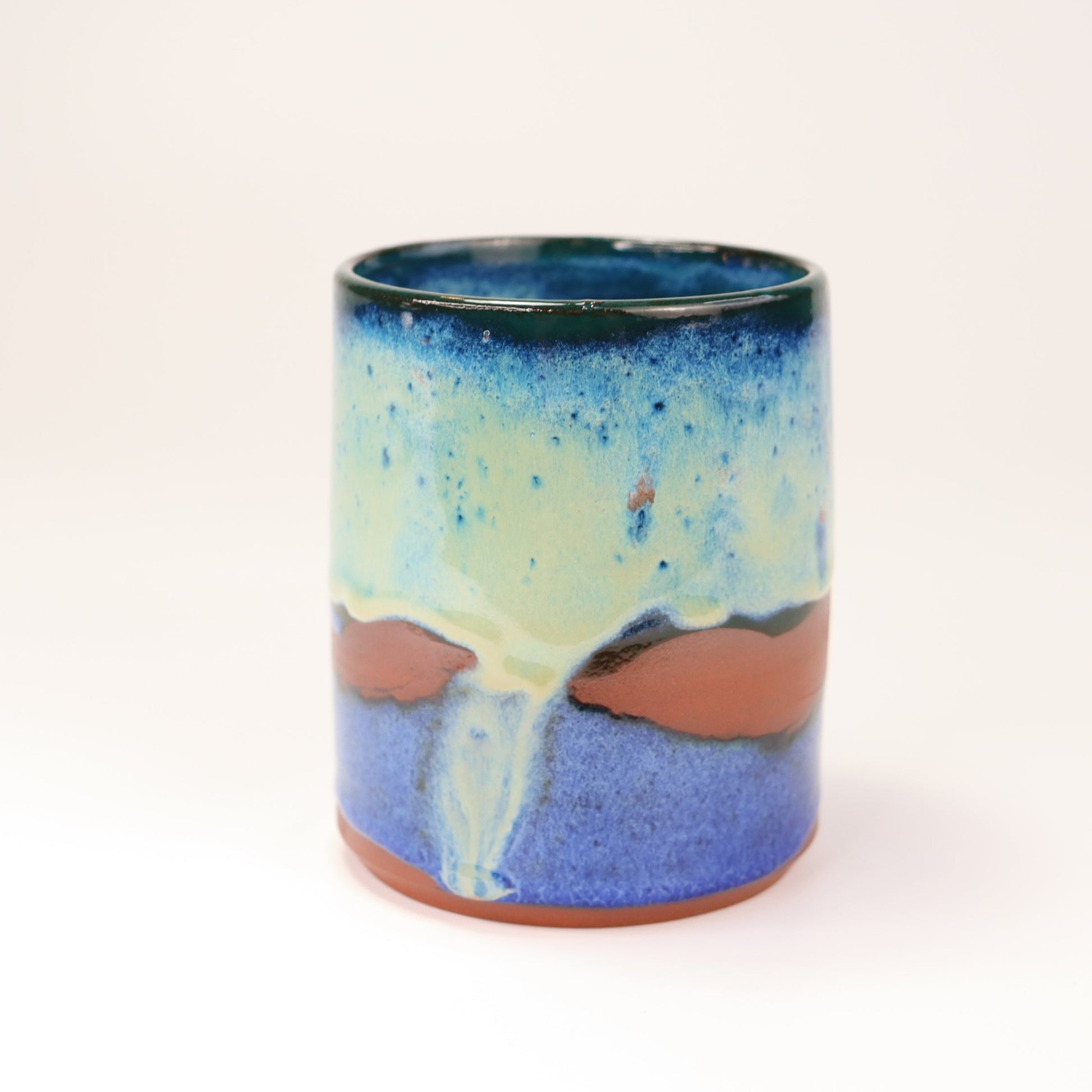 Handmade, wheel thrown highball style cup glazed in blues, teals and greens. I've deliberately left bare bands in a random fashion around the middle of the pot to reveal he deep red/burgundy clay body in a unique bikini-eques style.