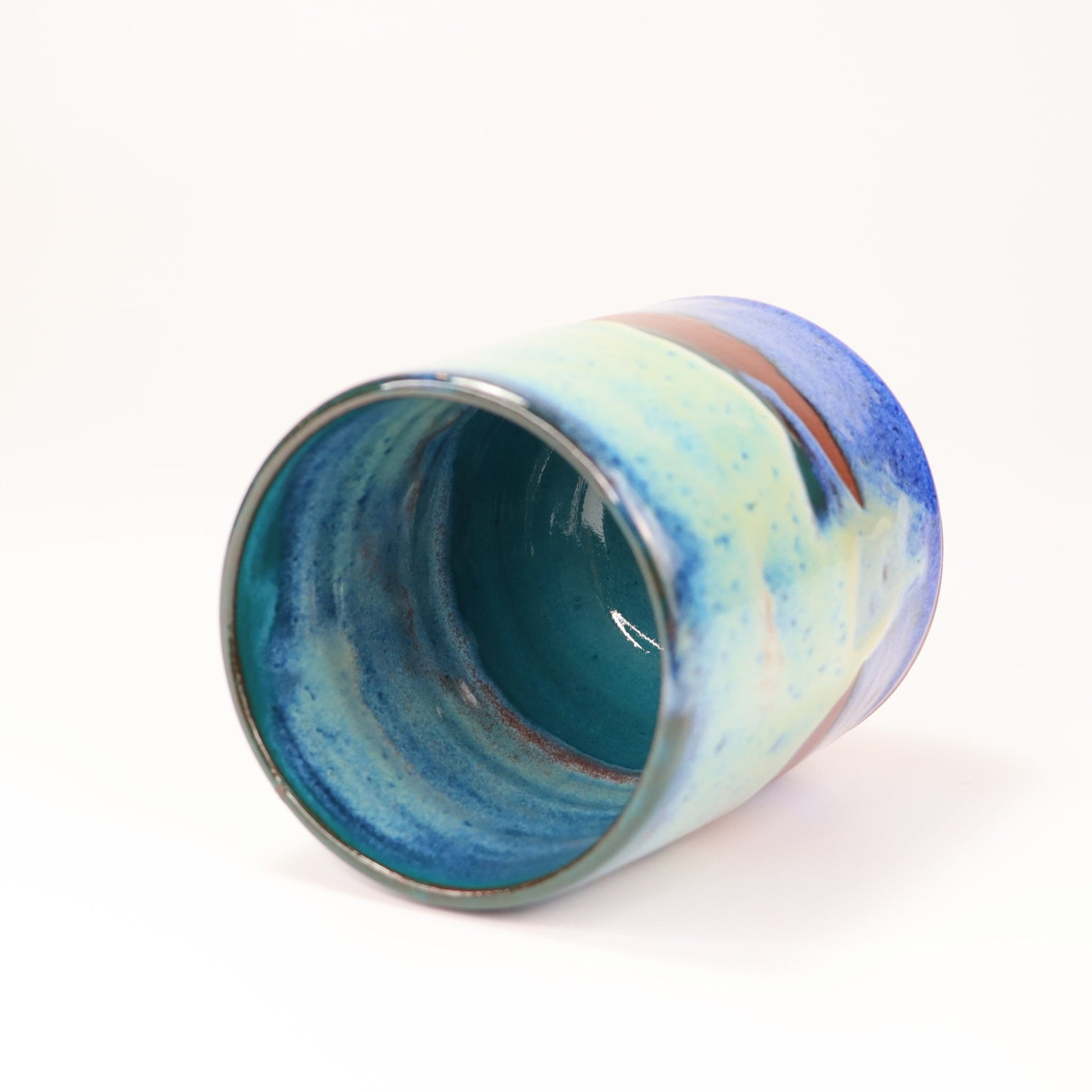 Handmade, wheel thrown highball style cup glazed in blues, teals and greens. I've deliberately left bare bands in a random fashion around the middle of the pot to reveal he deep red/burgundy clay body in a unique bikini-eques style.